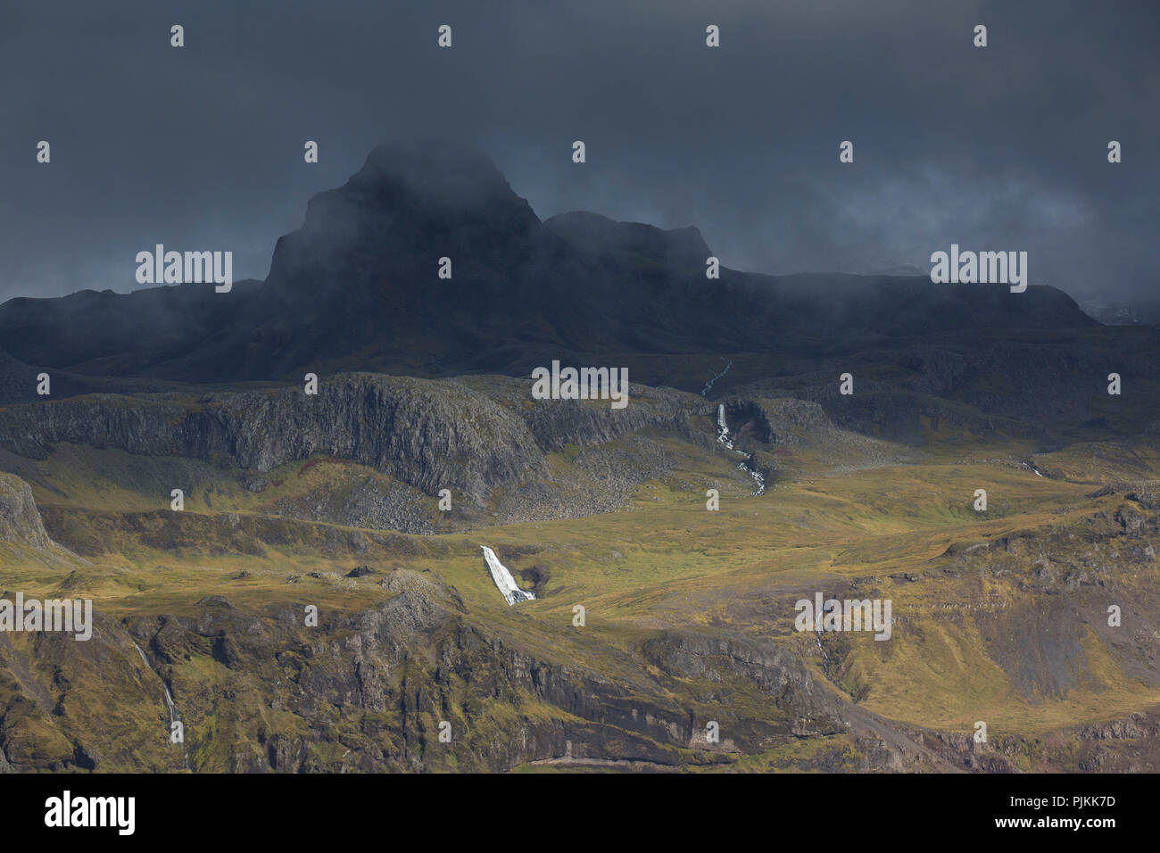 L'Islande, péninsule de Snæfellsnes, sombre, noir nuages sur la pente ensoleillée, cascades, Banque D'Images