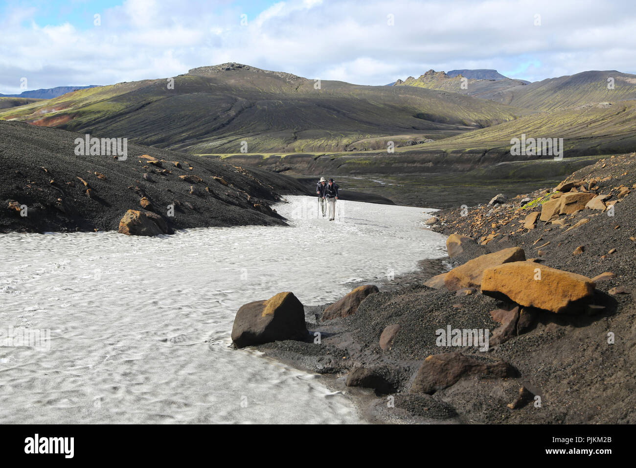 L'Islande, deux randonneurs sur un champ de neige dans le désert de lave, montagnes en arrière-plan, de sable noir et des pierres orange Banque D'Images