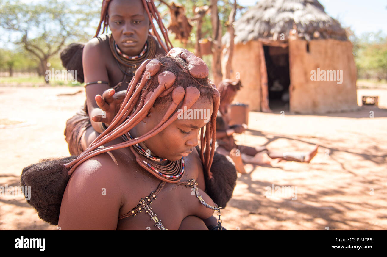 Les jeunes femmes Himba faire leurs cheveux. L'ocre, les cheveux des femmes est tordu dans tresses Banque D'Images Les jeunes femmes Himba faire leurs cheveux. L'ocre, les cheveux des femmes est tordu dans tresses Banque D'Images