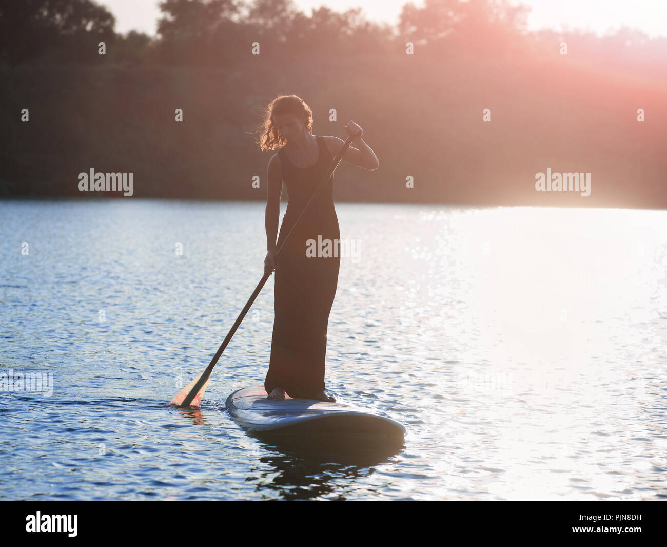 Silhouette d'une belle femme dans une robe noire sur stand up paddle board, le coucher du soleil. SUP Banque D'Images
