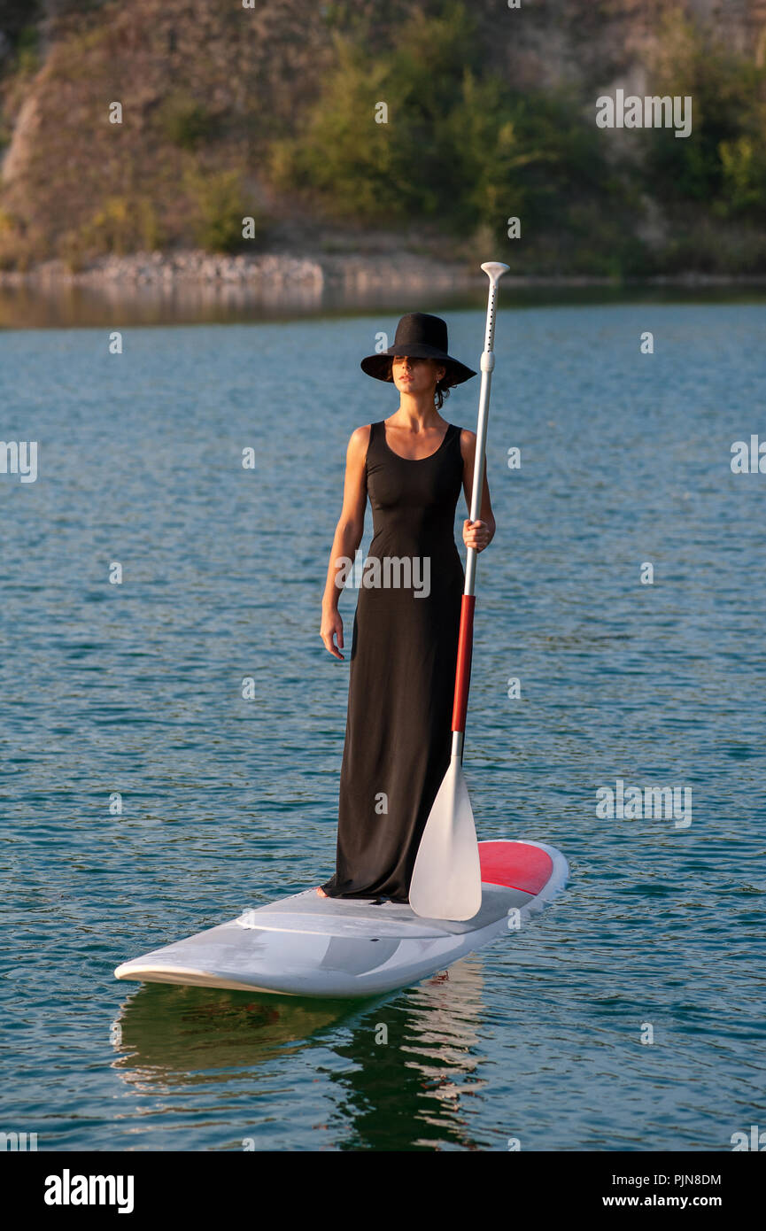 Silhouette d'une belle femme dans une robe noire sur stand up paddle board, le coucher du soleil. SUP Banque D'Images