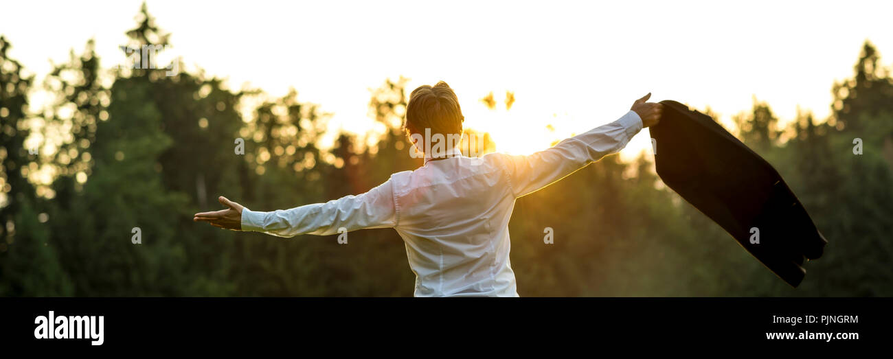 Businessman en chemise blanche debout avec ses bras étendu holding veste de costume dans une main célébrer la vie ou le succès par le contre-jour des rayons de l'aube Banque D'Images