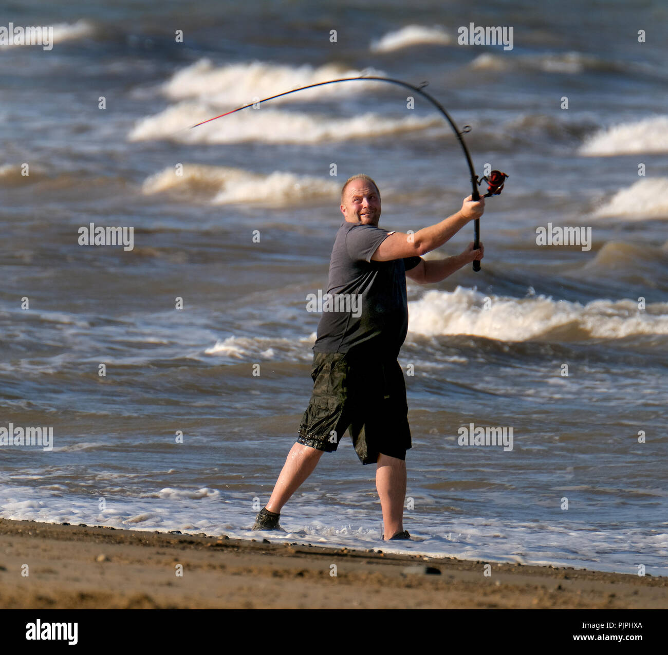 L'homme pêche en mer à partir de la plage, dans des conditions difficiles. Banque D'Images