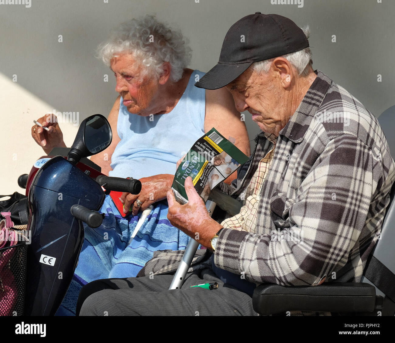 Vieil Homme et femme dans les scooters non valide fumeurs à l'extérieur dans le soleil. Banque D'Images