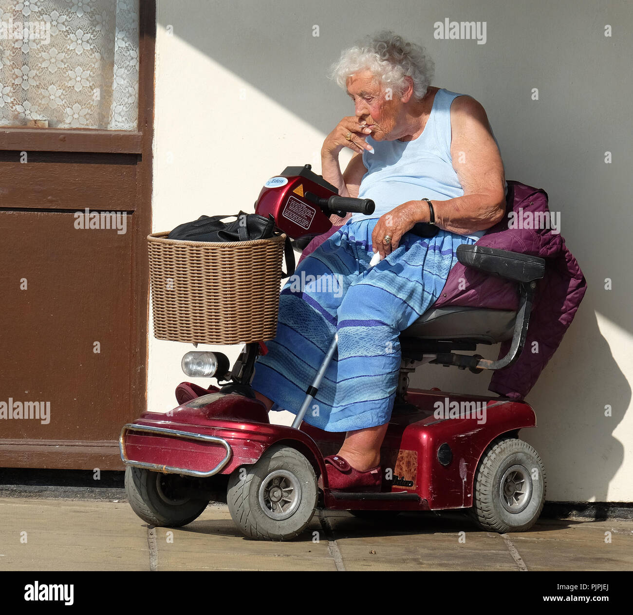 Vieille dame invalide sur cigarette scooter à l'extérieur dans le soleil. Banque D'Images