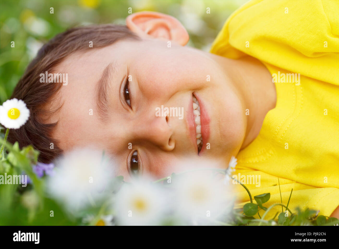 Kid enfant pré des fleurs de printemps fleurs petit garçon face à l'extérieur à l'extérieur extérieur portrait nature champ Banque D'Images