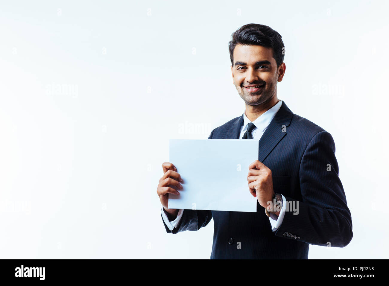 Portrait d'un homme en costume d'affaires, smiling, looking at camera, tenant un carton blanc avec les deux mains, isolated on white background studio Banque D'Images