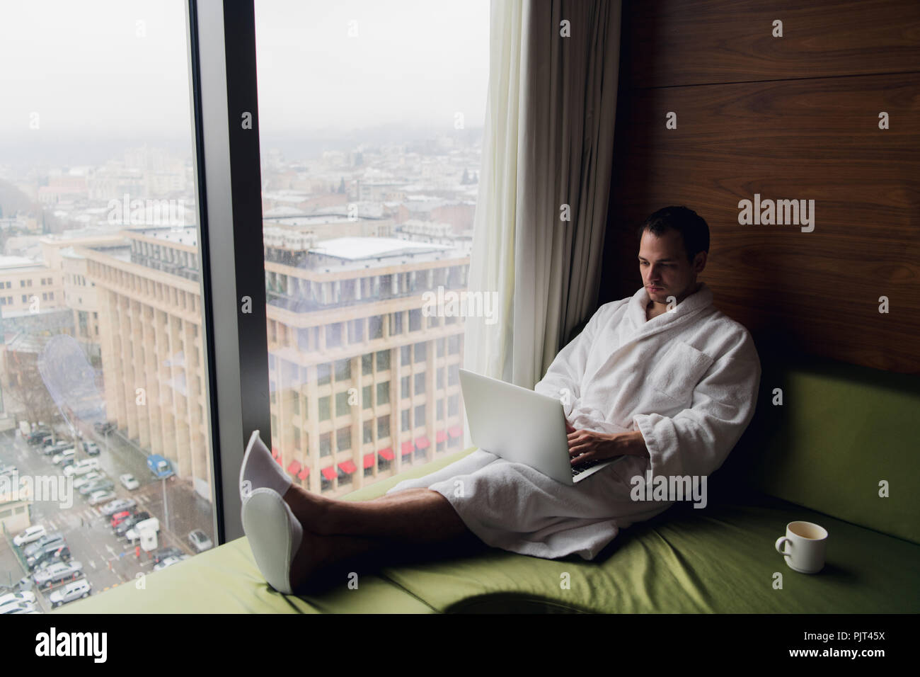 Homme heureux de boire du café et à l'aide d'ordinateur portable dans le lit le matin Banque D'Images