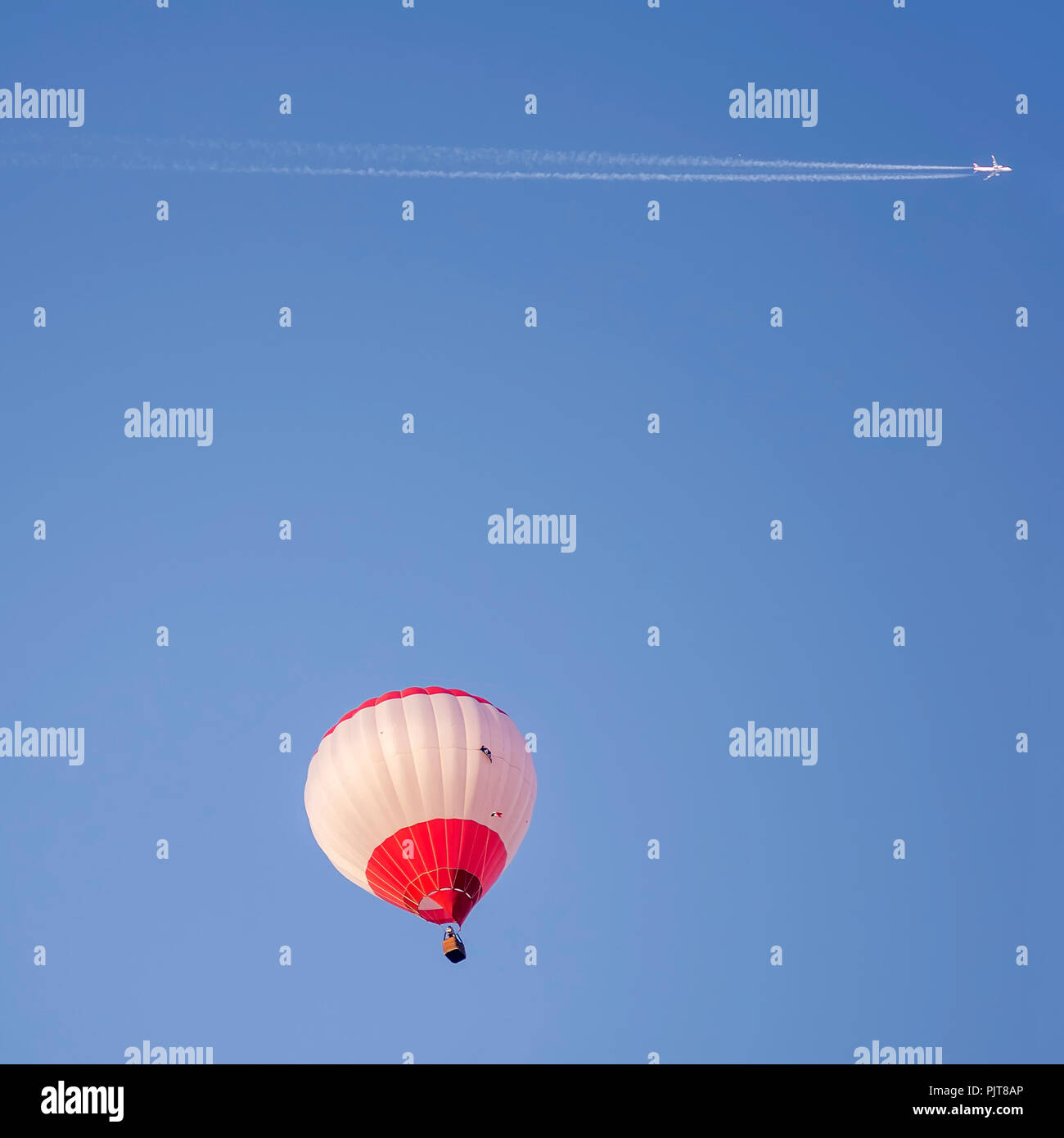 Avion à réaction avec une longue piste blanche survole un ballon à air chaud dans un beau ciel bleu Banque D'Images