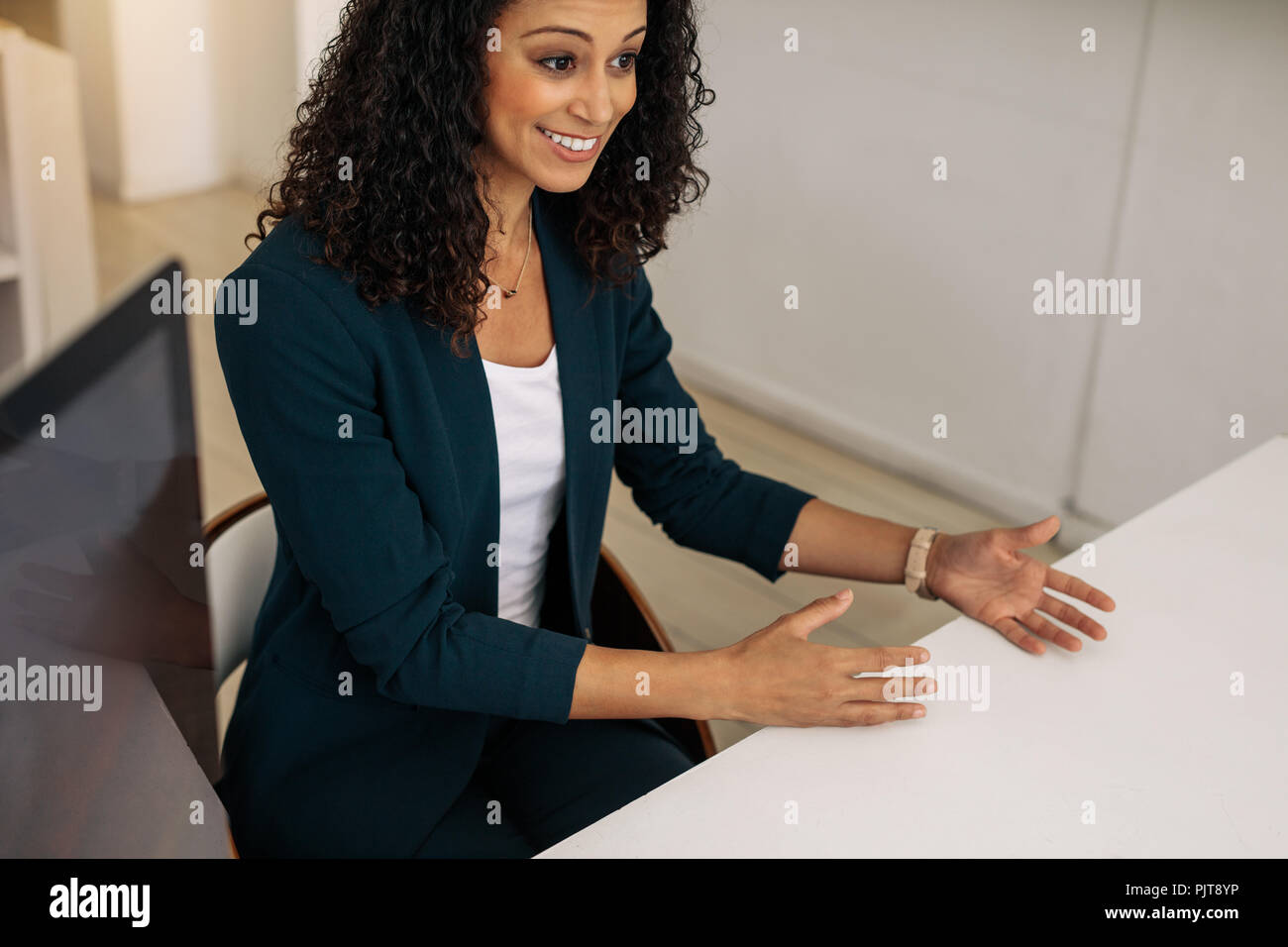 Femme d'affaires souriante assise dans le bureau faisant des gestes de la main tout en discutant du travail. femme d'affaires avec des cheveux bouclés dans des vêtements formels dans une réunion à lui Banque D'Images