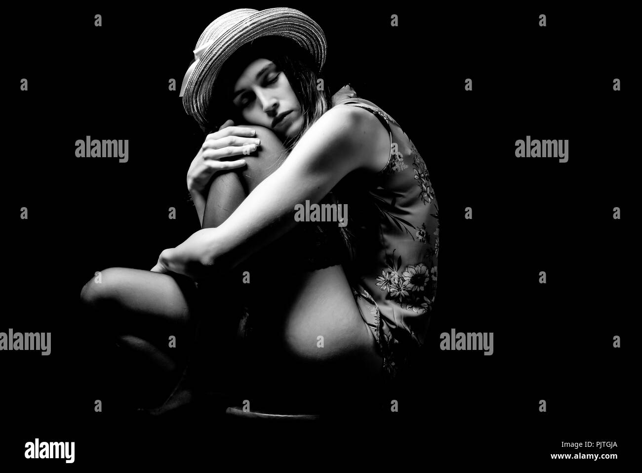 Un studio image d'une jeune femme assise sur un tabouret serrant ses genoux contre sa poitrine, à la triste Banque D'Images