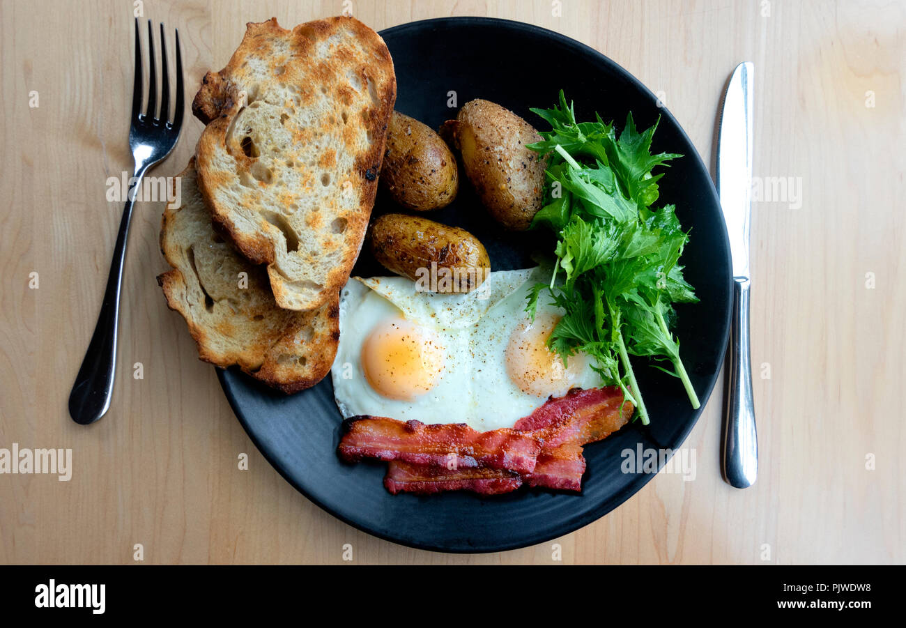 Deux œufs au plat, bacon, pommes de terre, pain grillé et verts rustic Banque D'Images Deux œufs au plat, bacon, pommes de terre, pain grillé et verts rustic Banque D'Images