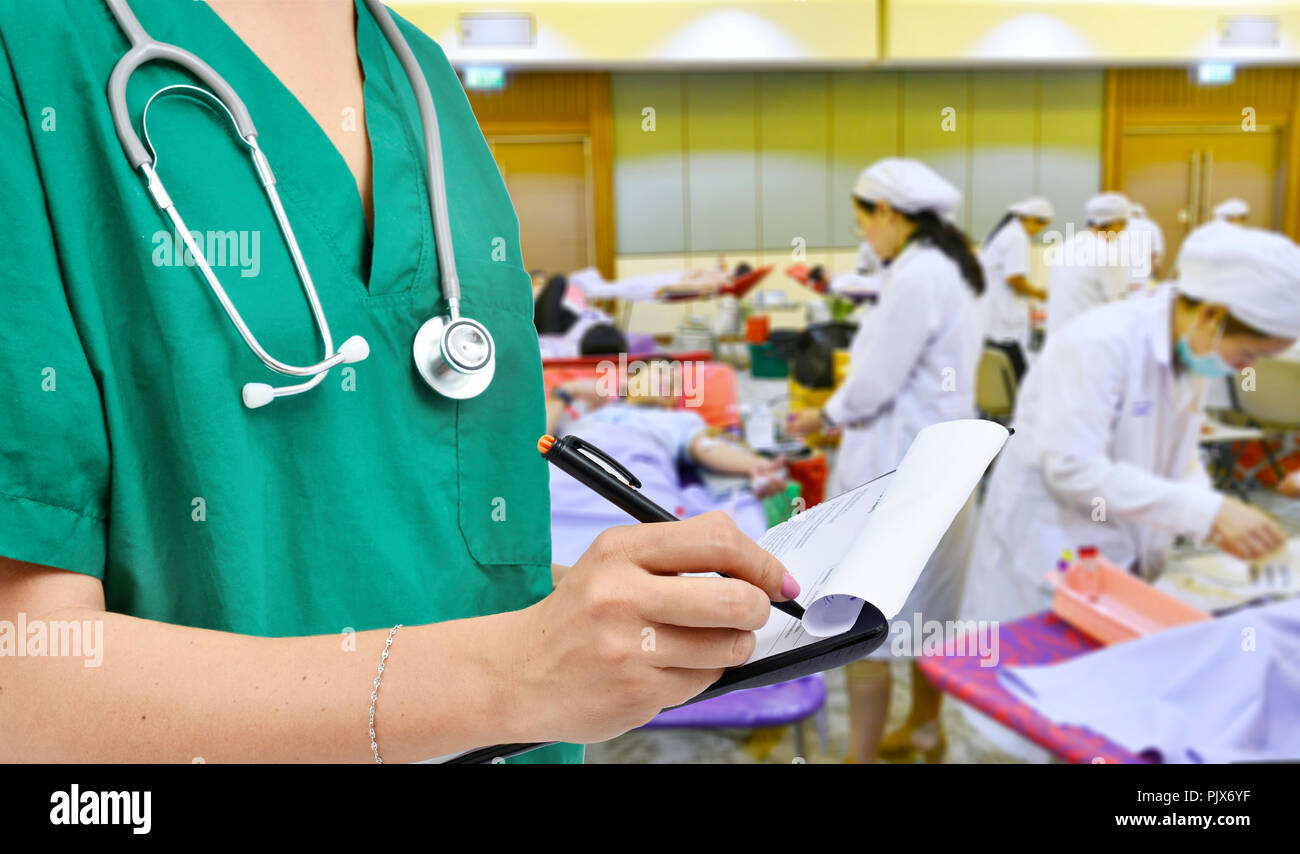 Médecin dans la chemise verte avec stéthoscope écrit le dossier patient et l'infirmière qui reçoit un don de sang à l'hôpital Banque D'Images