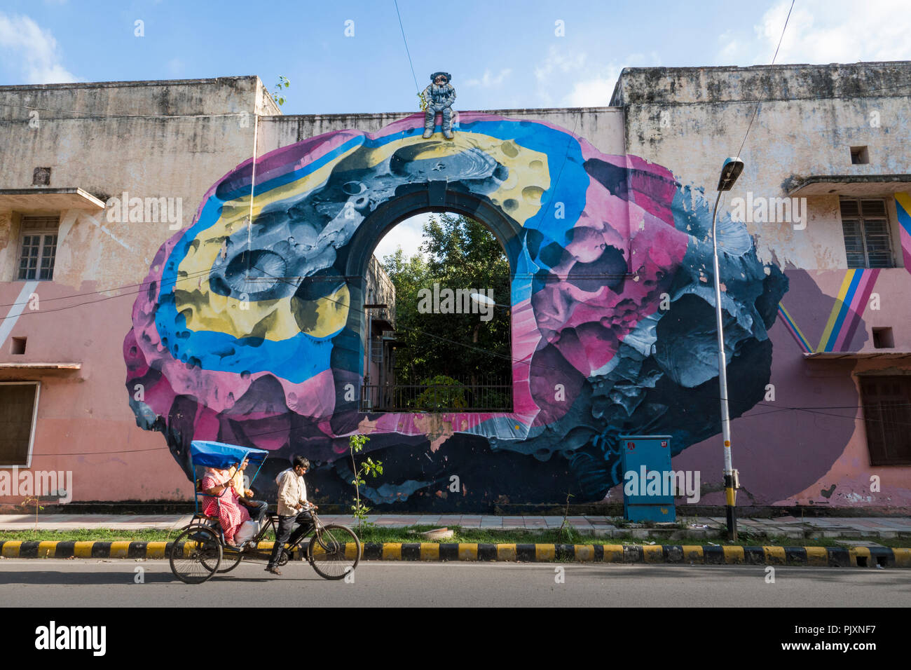 Rickshaw ride rider et passager passé wall mural sur bâtiment peint par des artistes suisses NeverCrew dans Lodhi colony, New Delhi, Inde Banque D'Images
