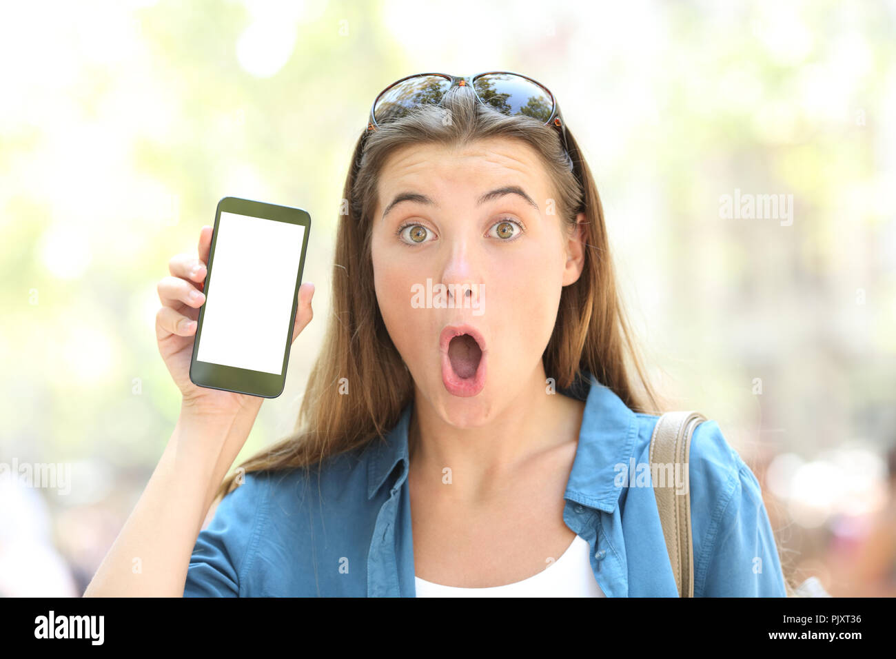 Vue avant, portrait d'une jeune fille surprise montrant un écran de téléphone à puce vierges à l'extérieur dans la rue Banque D'Images