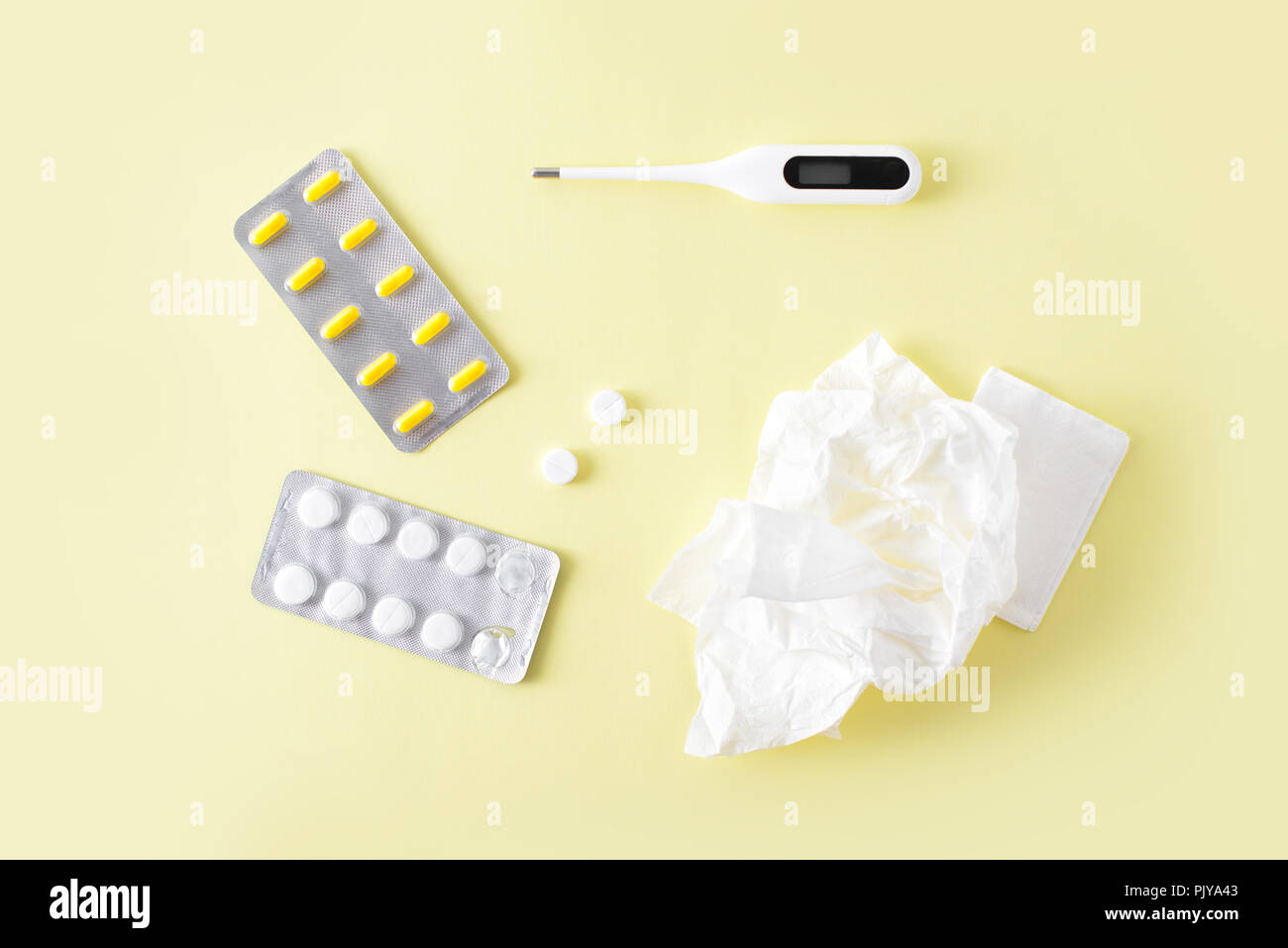 Pilules, serviettes pour le nez et thermomètre sur fond jaune. Le traitement du rhume et de la grippe. Mise à plat, vue du dessus. Banque D'Images