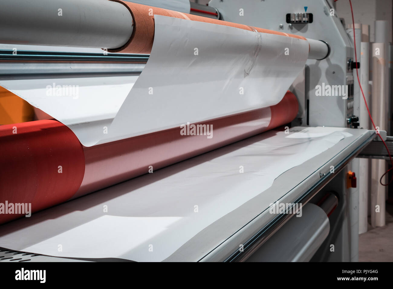 Big l'impression professionnelle d'enduction, armés de grands rouleaux de papier rouge brillant et de petits tubes de film transparent. Banque D'Images