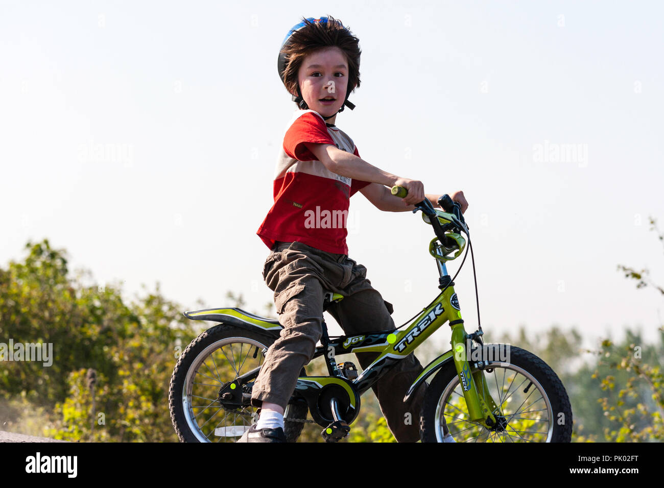 Caucasien enfant, garçon, 7-8 ans, le port d'un casque bleu et assis sur les petits enfants's Bike, le visage tourné vers le regard à l'afficheur. L'expression heureuse. Banque D'Images