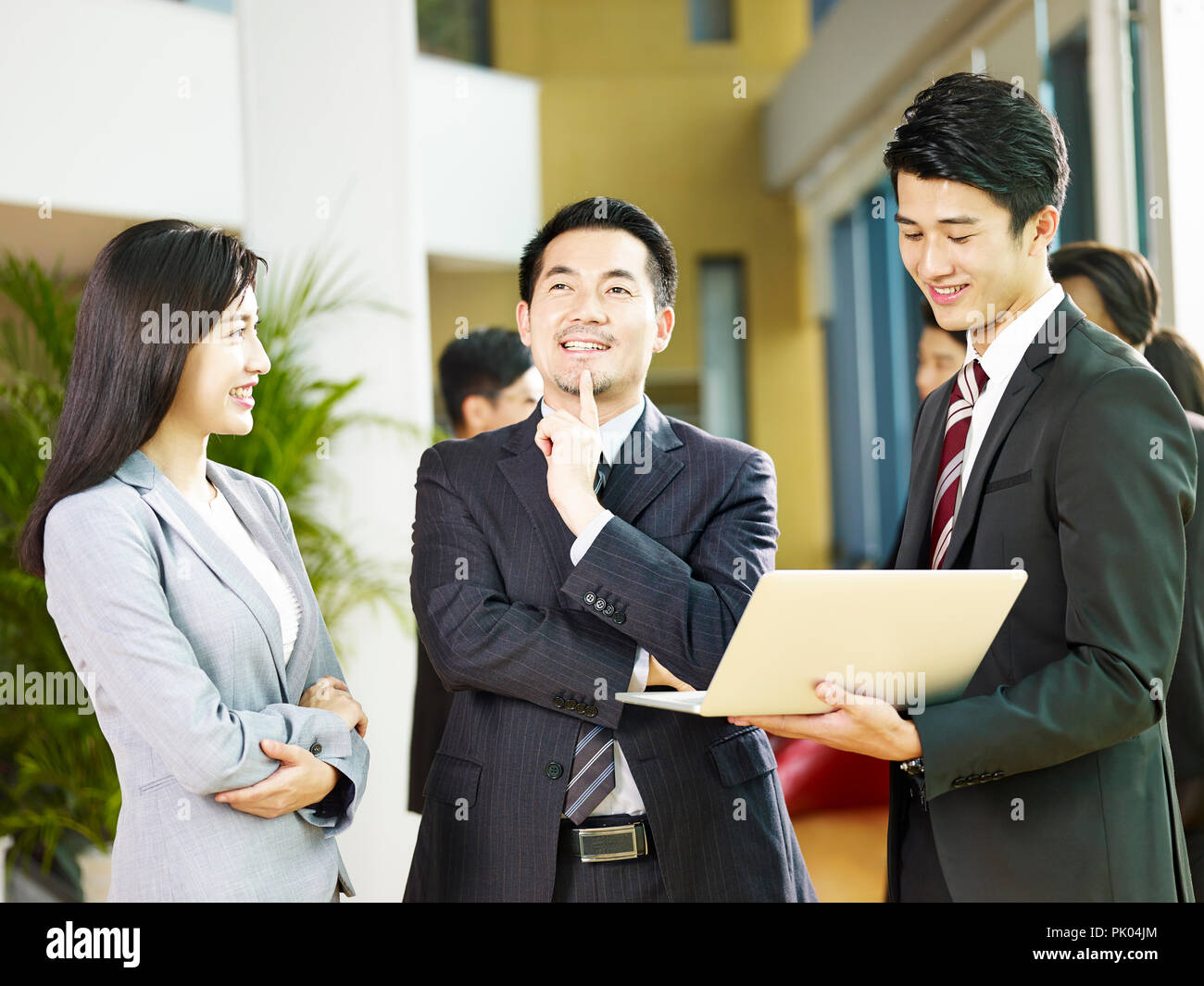 Deux hommes d'Asie et d'une femme d'affaires de discuter affaires à l'aide d'un ordinateur portable dans le hall de l'entreprise. Banque D'Images