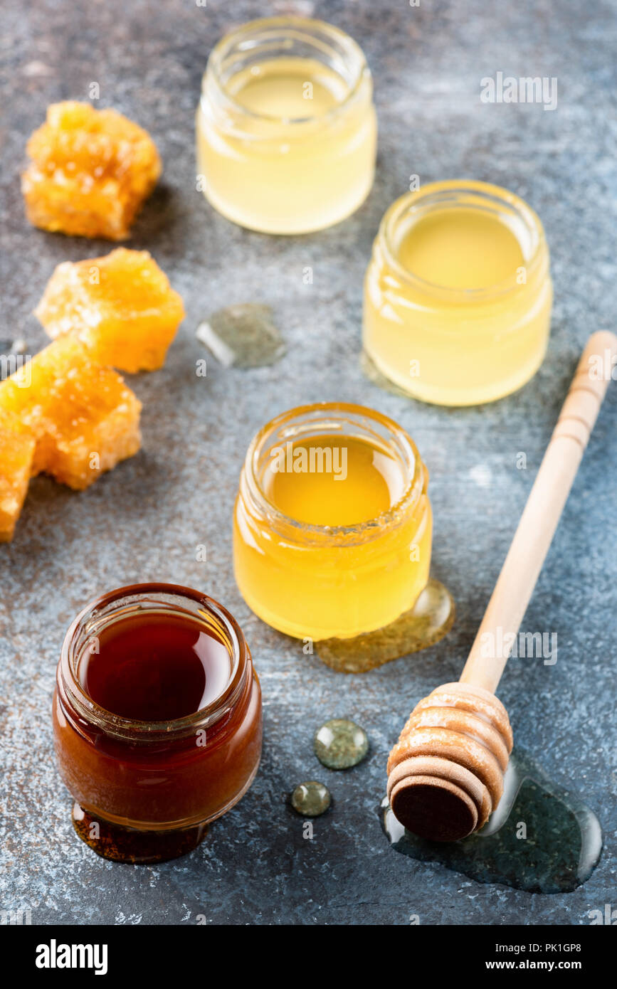 Différents types de miel. Acacia, miel de sarrasin, sauvages et de miel brut dans de petits pots de miel en bois balancier sur fond sombre Banque D'Images