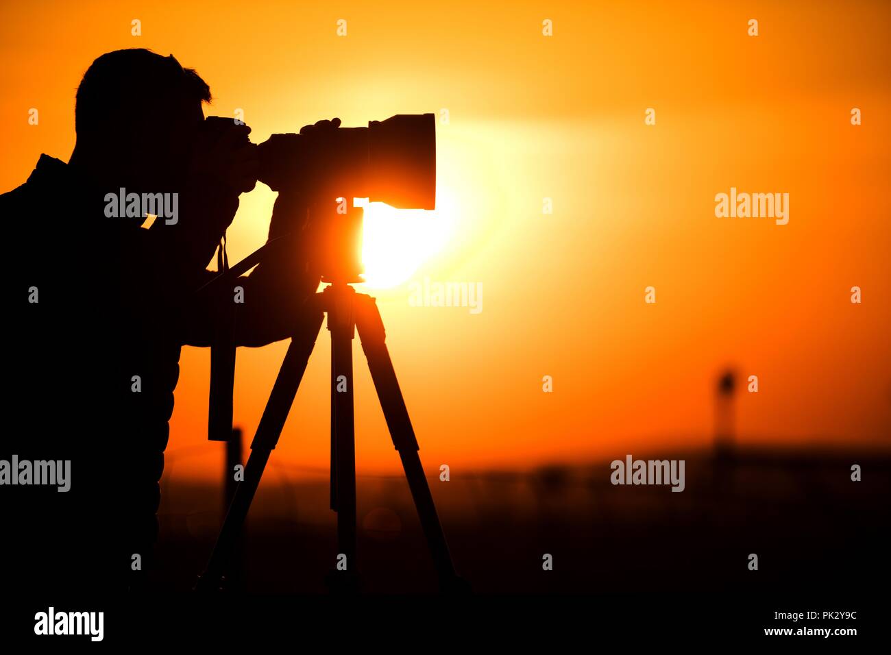 Silhouette d'amateur de photographie avec l'appareil photo sur un trépied pendant le coucher du soleil. Banque D'Images