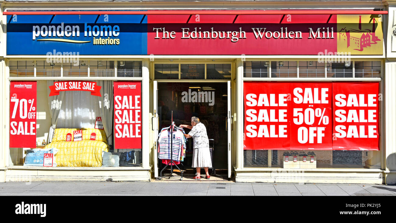 Old Lady shopping à tringle dans l'entrée de l'usine de laine Édimbourg high street magasin de vêtements au détail Vente posters shop UK Essex Brentwood vitre avant Banque D'Images