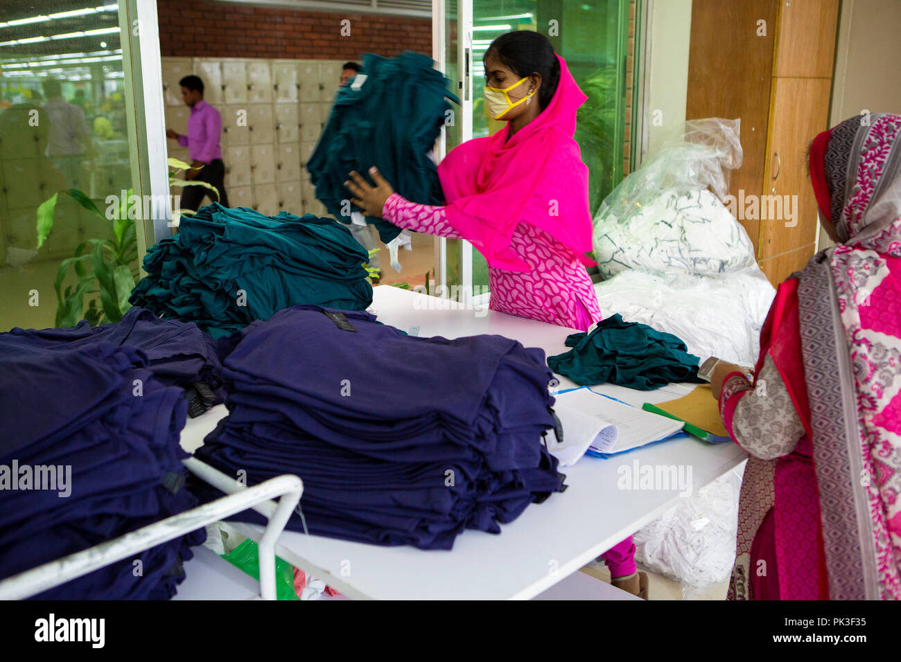 Une travailleuse du vêtement sorte via des piles de vêtements à l'intérieur d'une usine de confection au Bangladesh. Banque D'Images