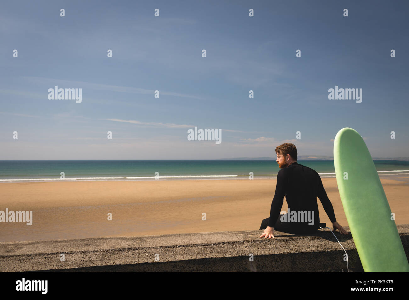 Surfer avec une planche de surf assis sur mur Banque D'Images Surfer avec une planche de surf assis sur mur Banque D'Images