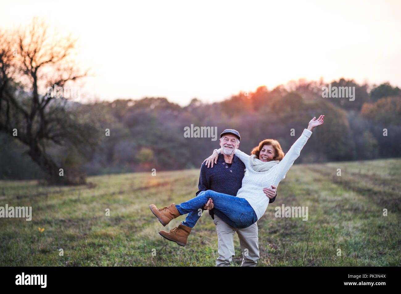 Hauts homme portant une femme dans ses bras dans une nature d'automne au coucher du soleil. Banque D'Images