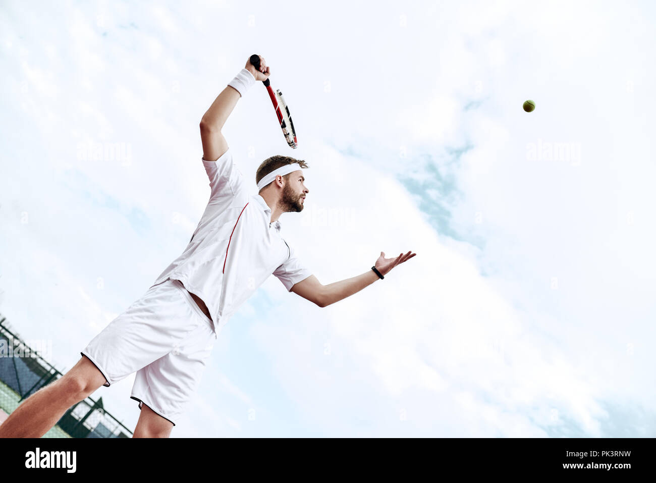 Joueur de tennis est en train de faire un coup de tennis sur un court de tennis sur un matin d'été ensoleillé. L'est habillé en vêtements de sport. Banque D'Images