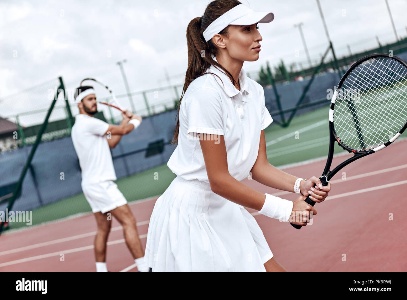 Ils jouent comme une équipe. Belle jeune femme holding tennis racket et à l'écart en se tenant sur le court de tennis et avec l'homme dans l'arrière-plan Banque D'Images