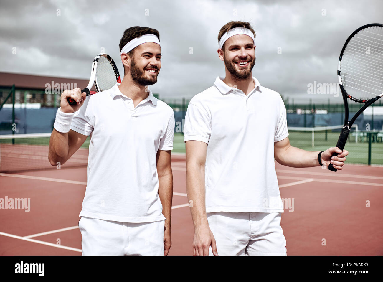 Partenariat d'affaires, et le sport. Partenaires d'affaires la pratique du sport ensemble. Les jeunes hommes la marche et à la recherche à court de tennis devant un jeu de tennis Banque D'Images