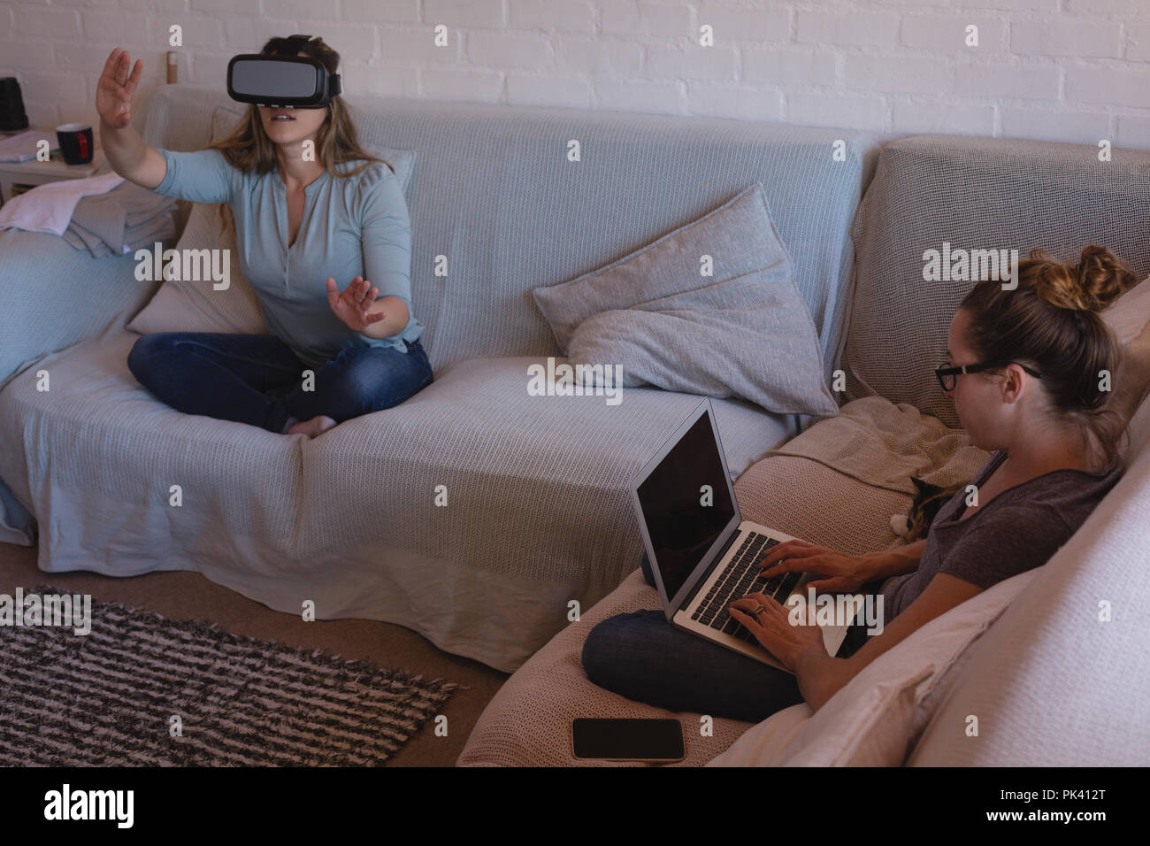Couple de lesbiennes à l'aide de casque de réalité virtuelle et de l'ordinateur portable sur canapé Banque D'Images