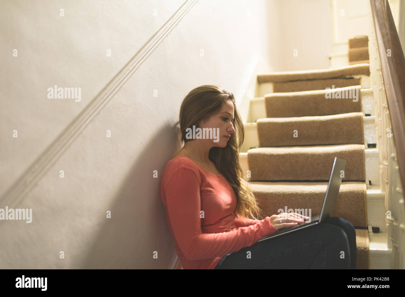 Woman using laptop on staircase at home Banque D'Images