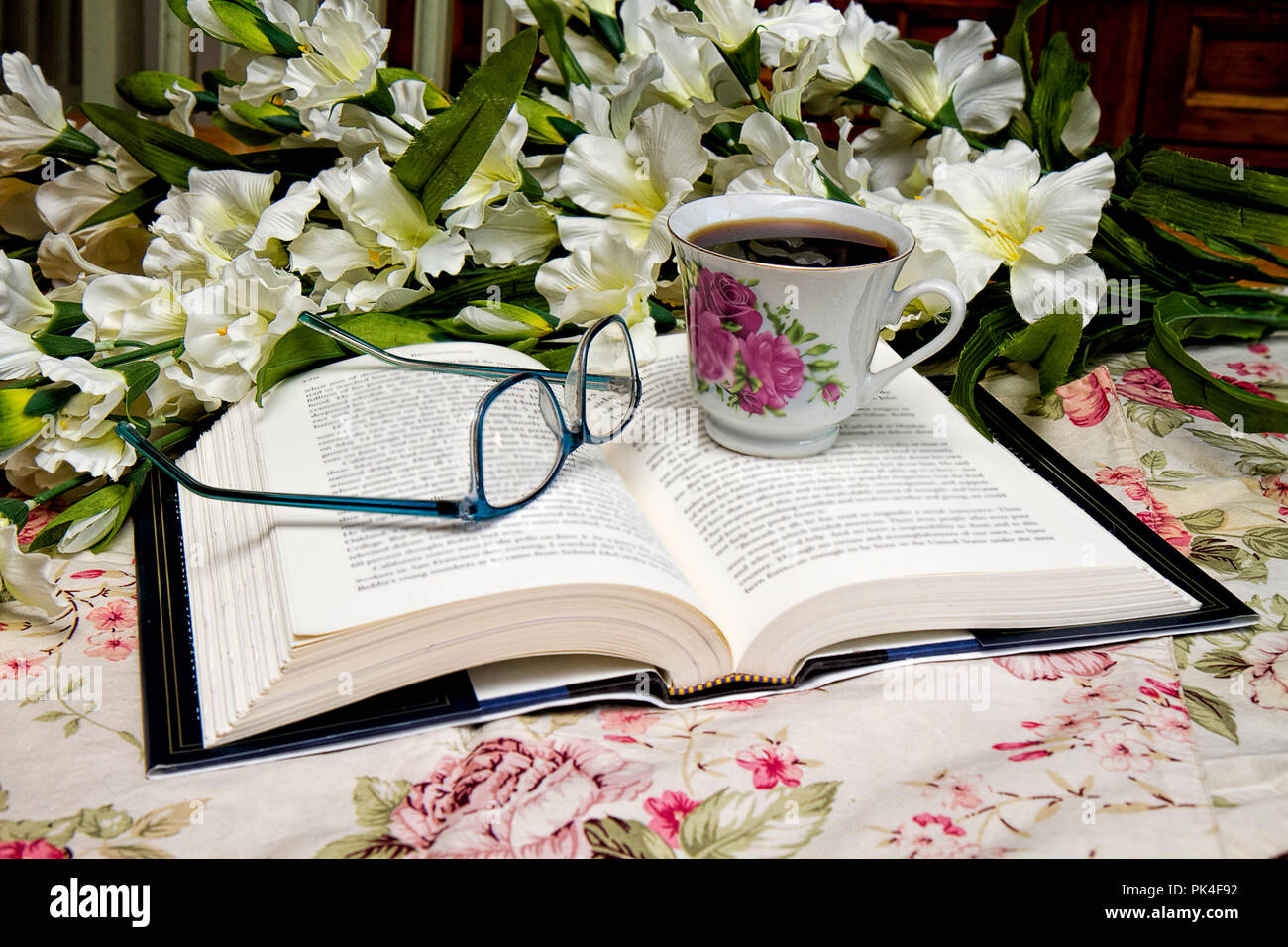 Livre ouvert avec paire de lunettes et une tasse de café assis à côté d'elle pendant la lecture. Bouquet de fleurs dans l'image. Banque D'Images