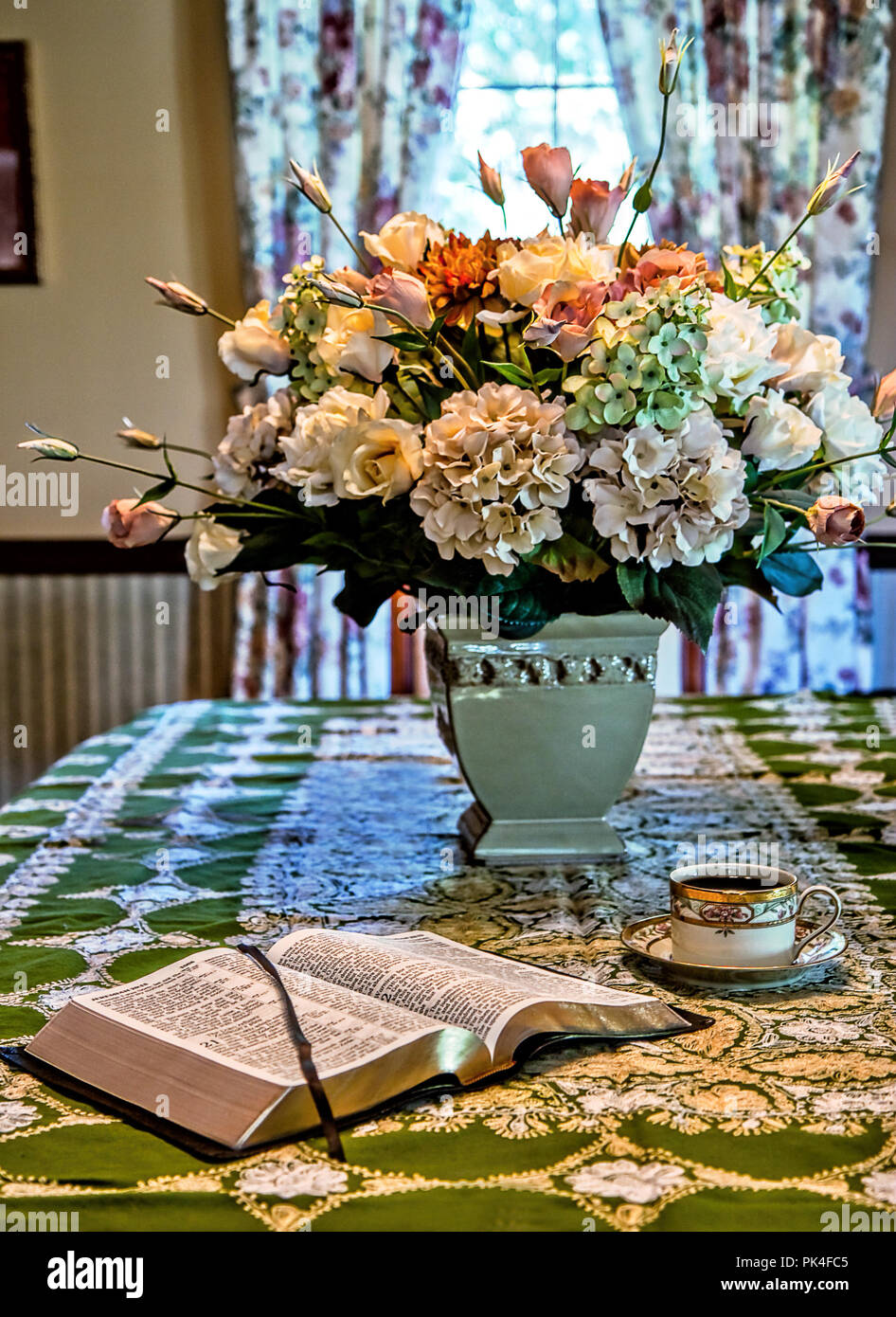 Bible ouverte assis avec tasse de café à côté de lui alors que l'une des études. Grand bouquet de fleurs sur la table de salle à manger et une fenêtre à l'arrière-plan. Banque D'Images