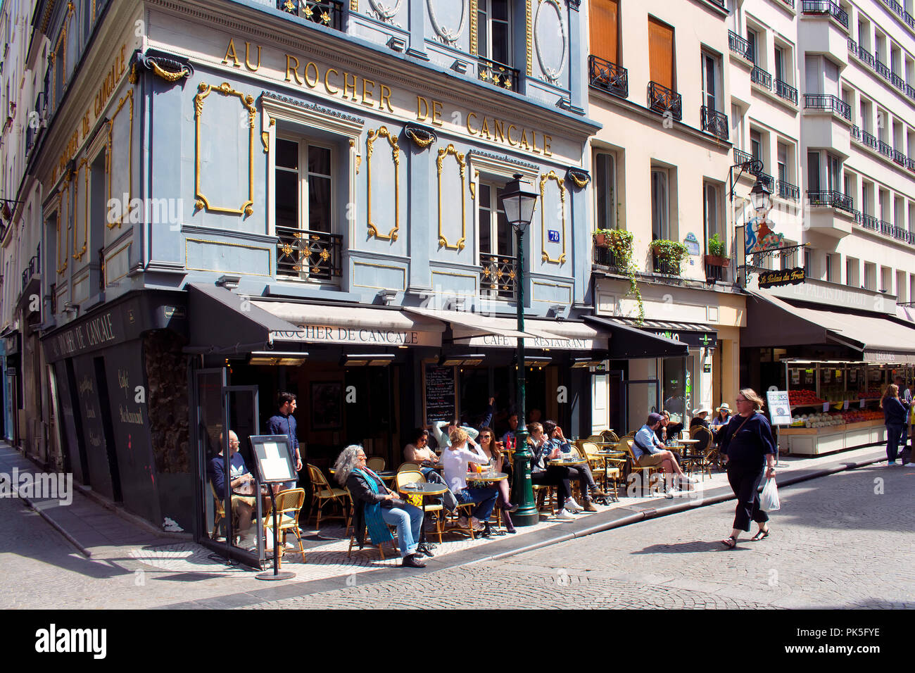Les gens profiter du beau temps dans un bistrot traditionnel / café sur l'une des célèbres rues (rue Montorgueil) à Paris. Femme passe. Banque D'Images