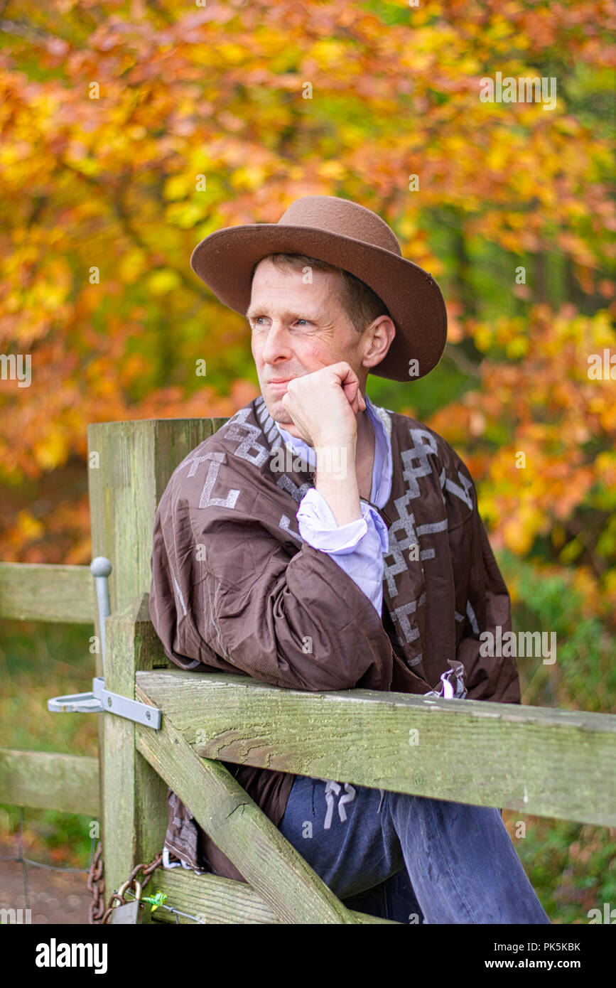 A middle aged man wearing a cowboy hat allongé contre un poteau de clôture. Banque D'Images