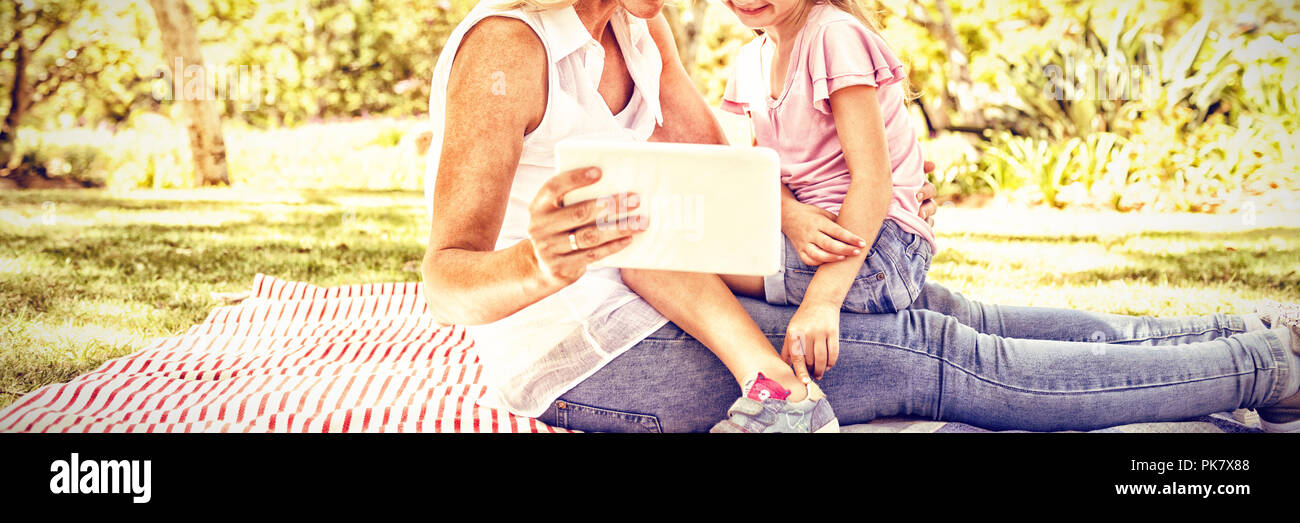 Happy mother and daughter using digital tablet in park Banque D'Images