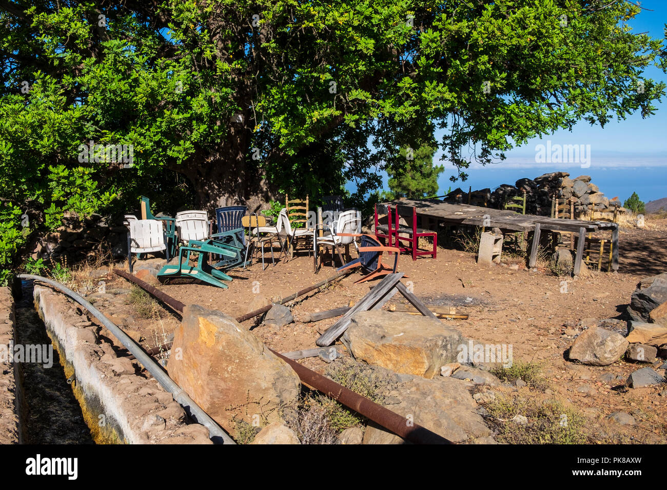 Collection de vieux fauteuils et d'une table de fortune par un arbre et un canal d'eau dans une région isolée dans les montagnes de Guia de Isora, probablement un repos, l Banque D'Images