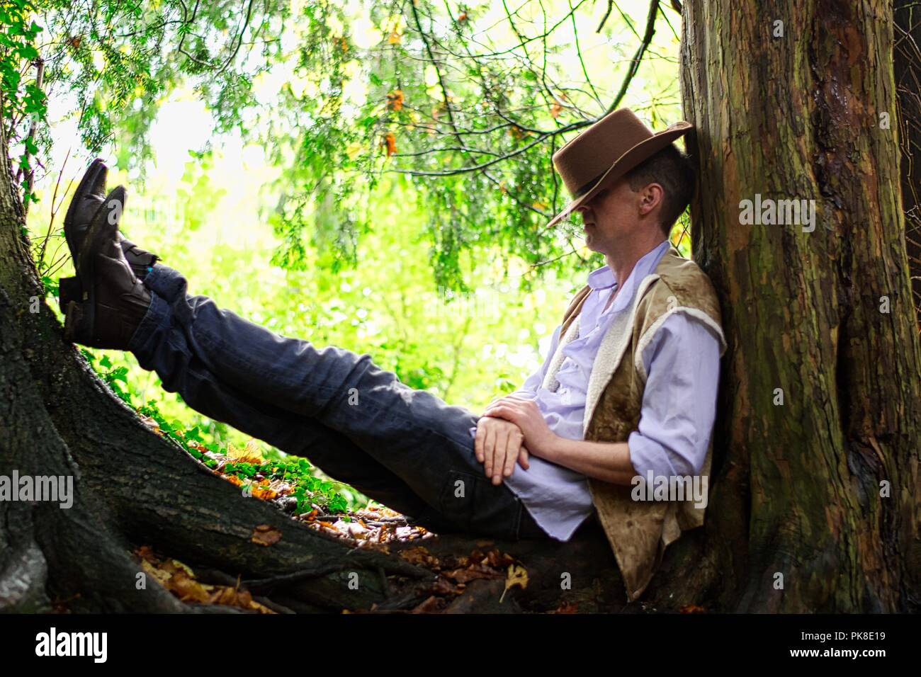 Un homme habillé comme un cowboy repose contre un tronc d'arbre Banque D'Images
