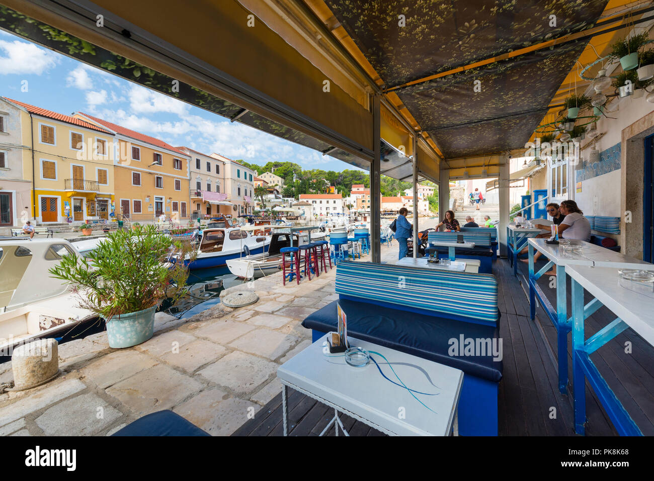Les gens sont assis dans un bar du port de Veli Lošinj avec bateaux de pêche en face de façades colorées, Lošinj, la baie de Kvarner, Croatie Banque D'Images