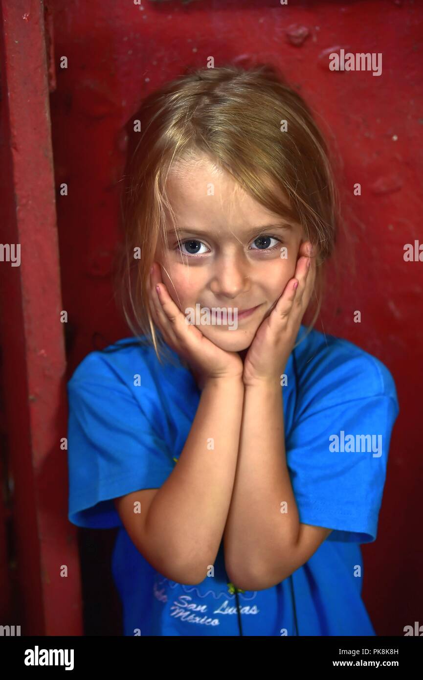 Portrait de belle petite fille sur fond de mur rouge. Petite fille blonde en souriant. Banque D'Images