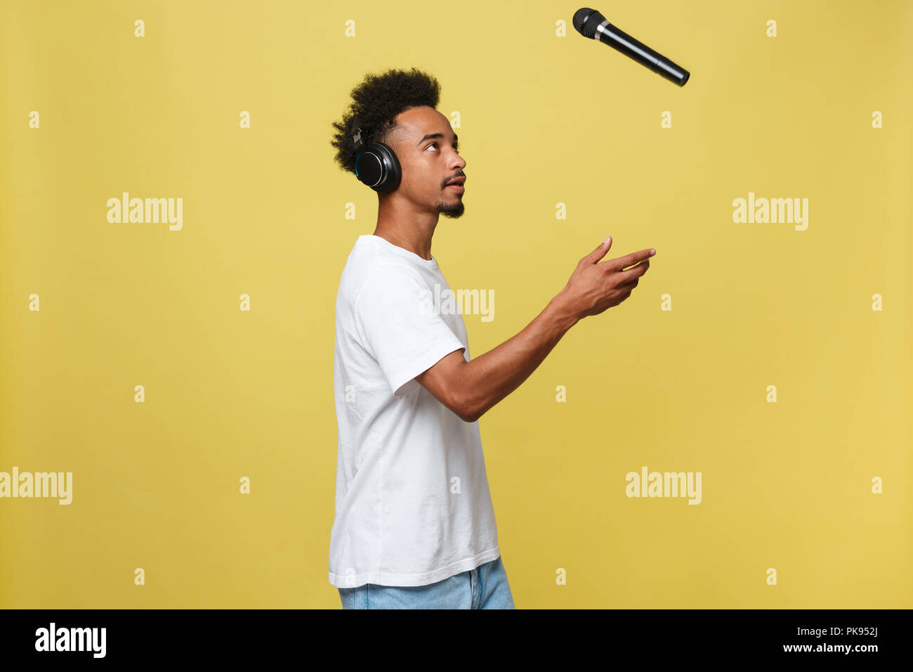 Beau Black man throwing un microphone et le chant. Sur un fond jaune isolé. Banque D'Images