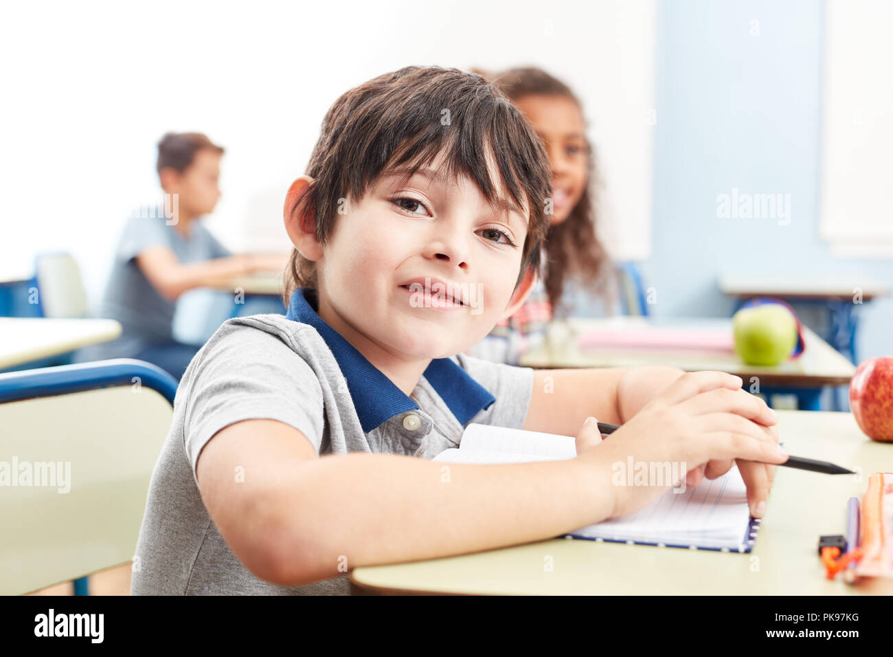 Smiling boy comme élève avec livre d'exercice tout en apprenant à l'école élémentaire Banque D'Images