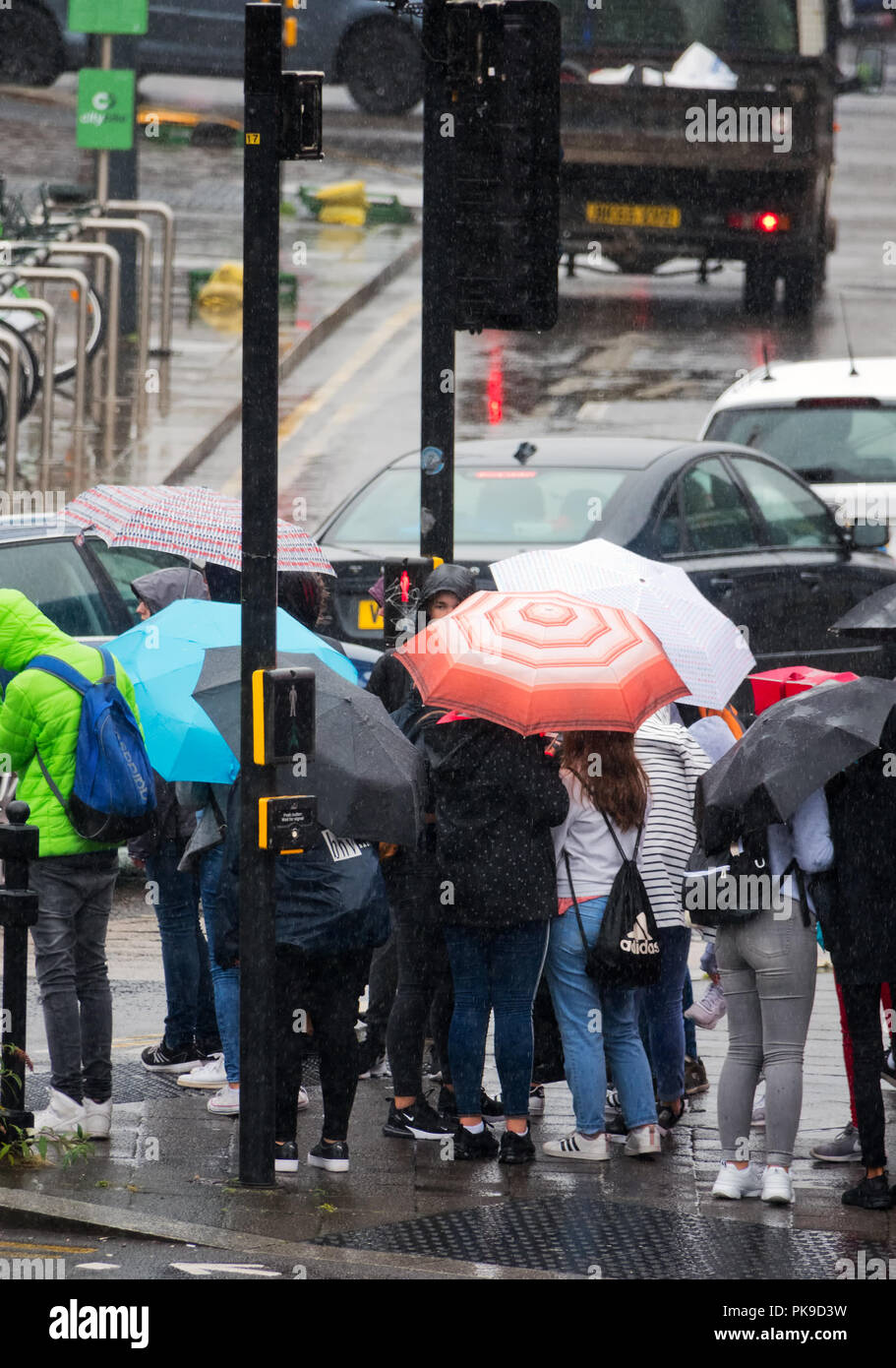 Météo britannique. Les gens sous les parasols pris dans une forte pluie douche tout en attendant de traverser la route à Liverpool UK. Banque D'Images