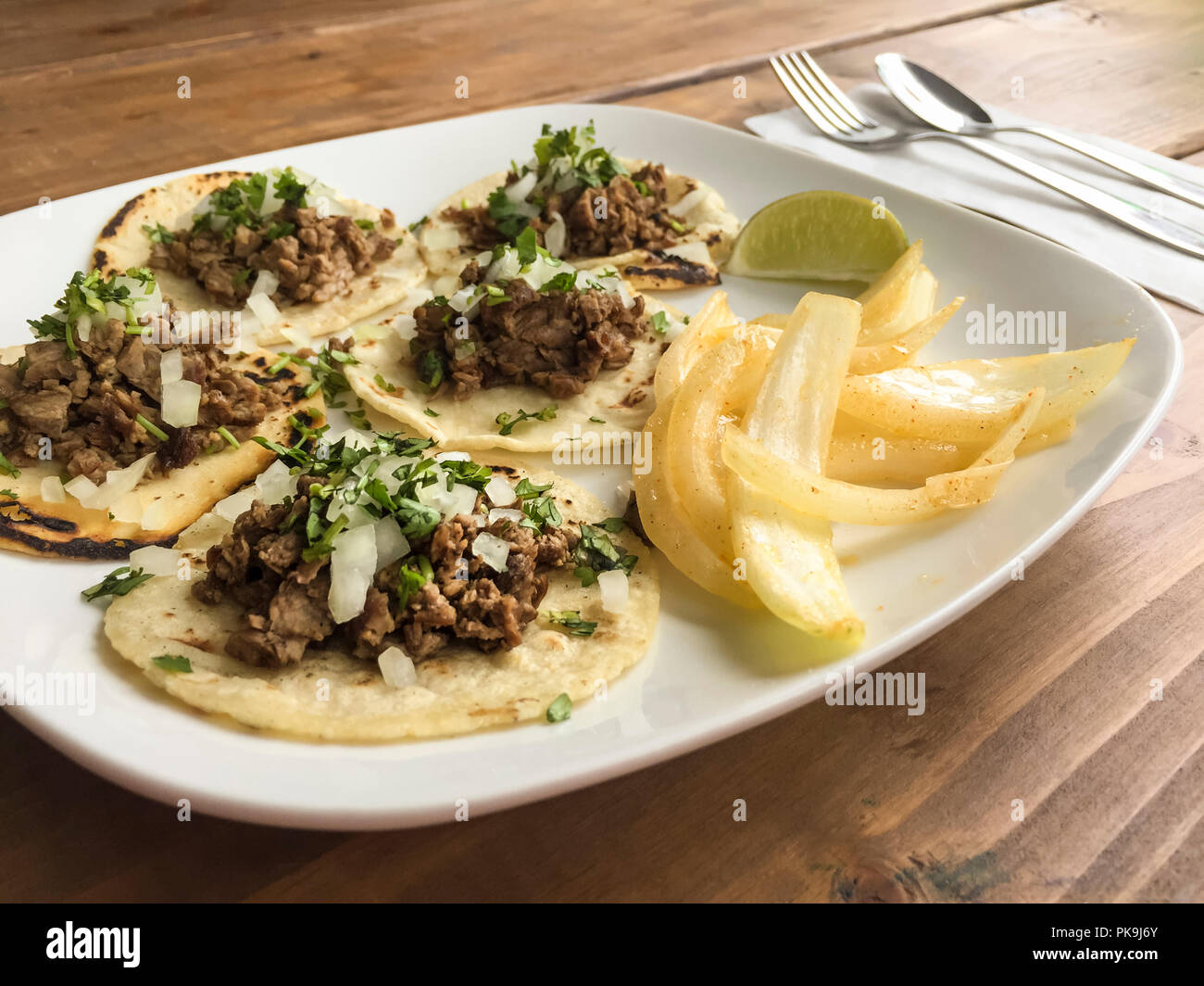 Les aliments mexicains traditionnels tacos fajitas boeuf grillé sur une plaque en céramique blanche avec tortilla de maïs, les oignons, la coriandre et lime garnir sur table en bois Banque D'Images