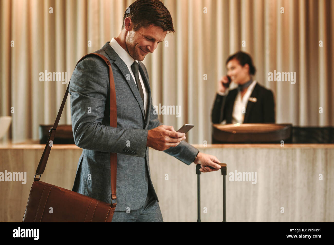Businessman walking in hotel lobby avec valise et à l'aide de son téléphone intelligent. Homme d'affaires dans l'hôtel couloir avec téléphone et assurance. Banque D'Images