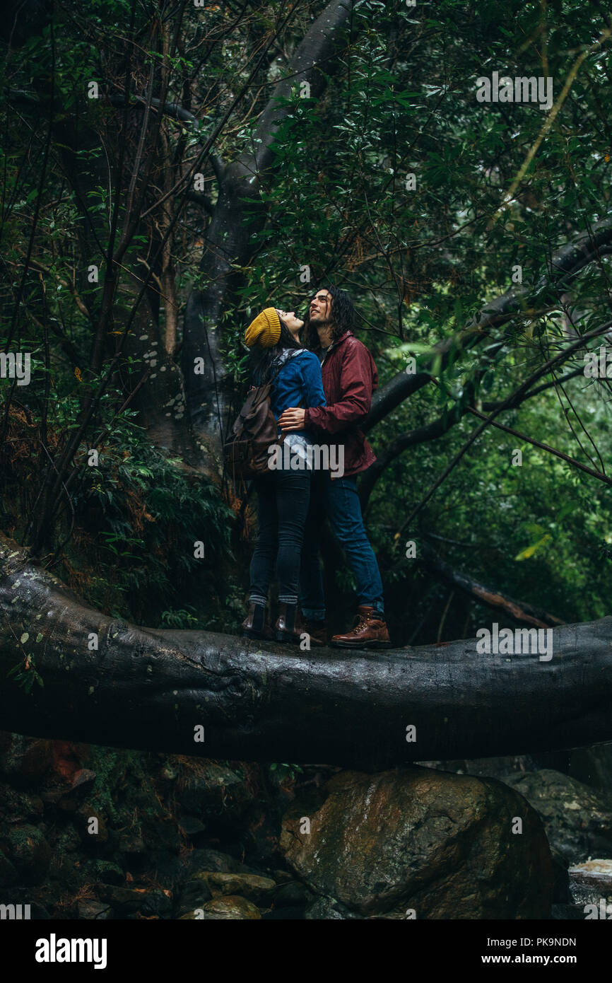 Jeune homme et femme enlacés tout en se tenant sur un journal à la forêt et profiter de la pluie. Couple en forêt se mouiller sous la pluie. Banque D'Images