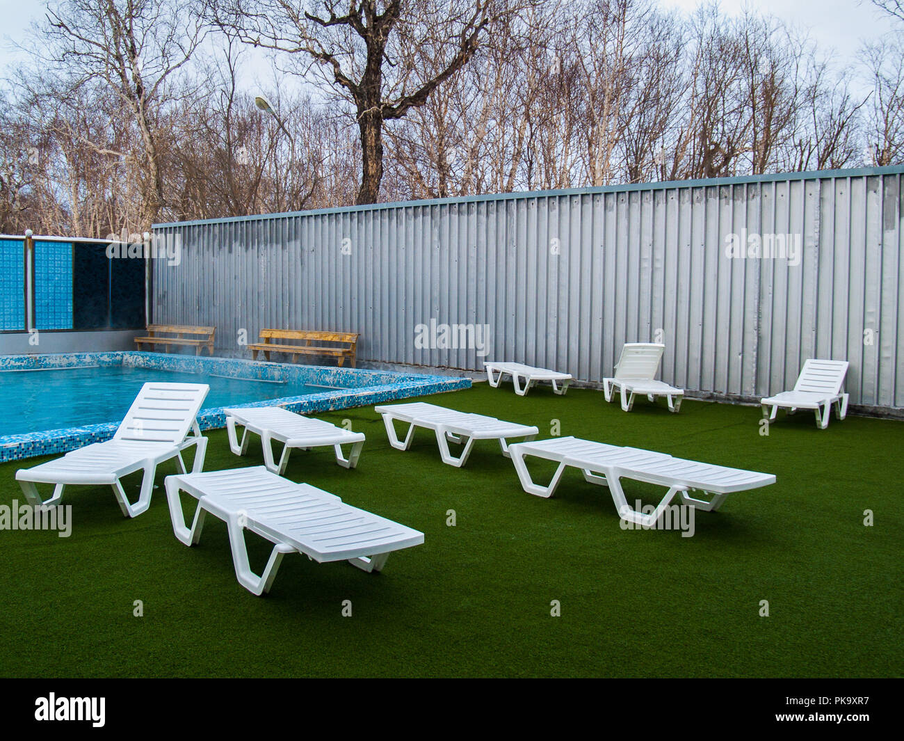 Des chaises longues en plastique blanc près de la piscine avec eau chaude thermale sur un terrain artificiel vert à Paratunka au Kamtchatka Banque D'Images